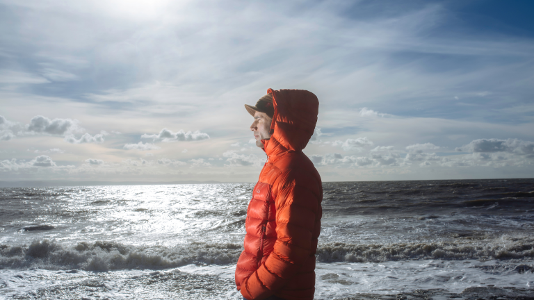 A man in an warm orange jacket looking out to sea