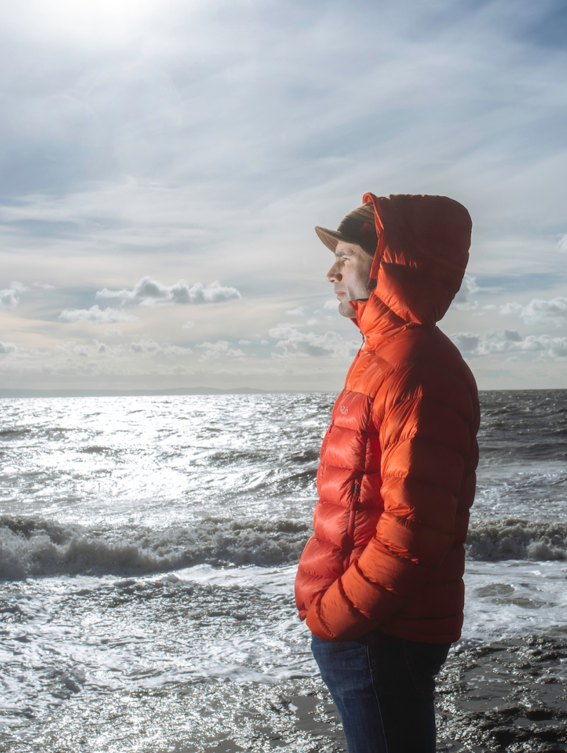 A man in an warm orange jacket looking out to sea