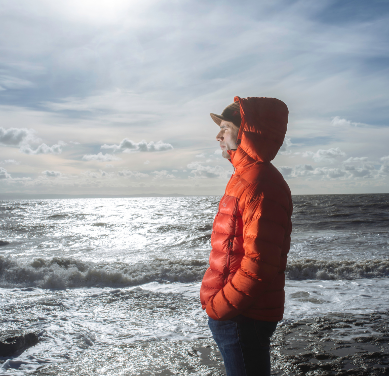 A man in an warm orange jacket looking out to sea
