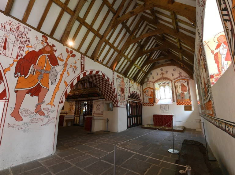 Interior of church with archways, murals on walls and wood on ceiling.