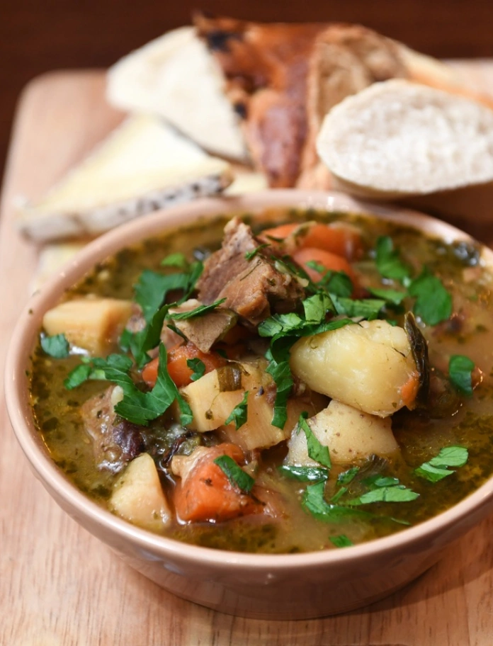 Un bol de cawl sur une planche à pain accompagné de pain.