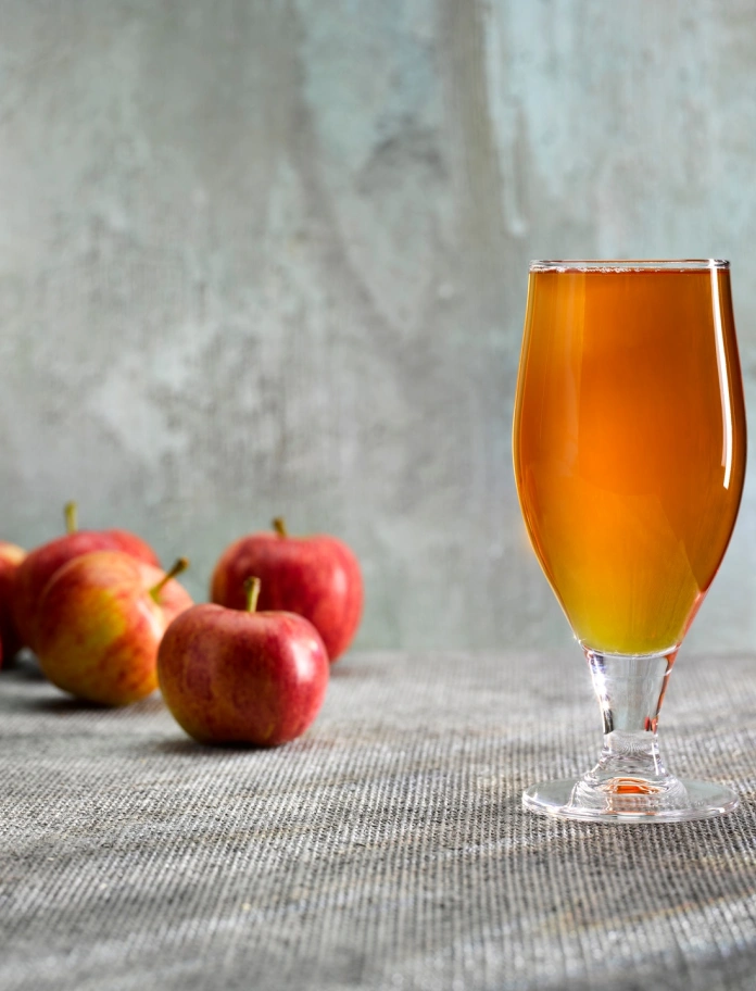 A glass of apple cider next to some apples.