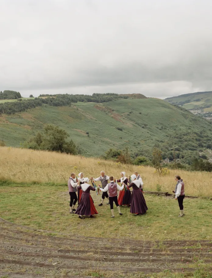 A group of dancers dressed in traditional outfits, dancing on a green hillside with valleys in the distance