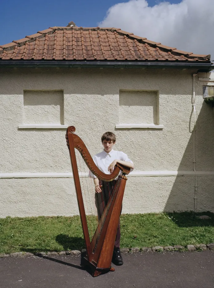 Harpist Cerys Hafana standing with her harp in front of Pontypridd Lido