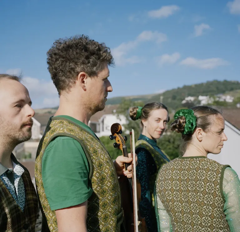 Four performers dressed in traditional Welsh garments standing outside against a blue sky