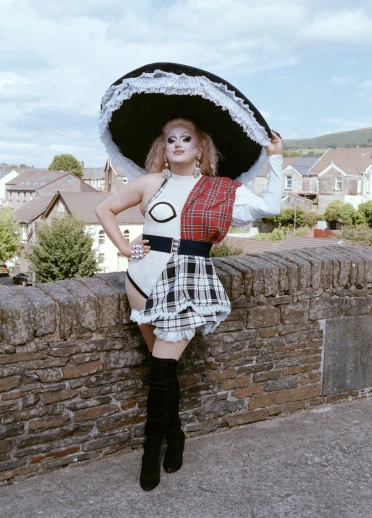 Drag queen Catrin Feelings dressed in a modern Welsh lady's outfit, standing on an old stone bridge