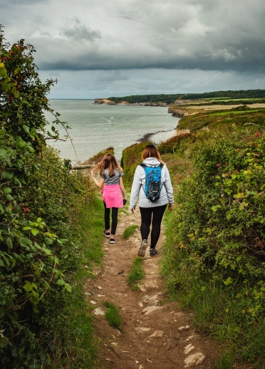 Two women walking down a path to the sea.