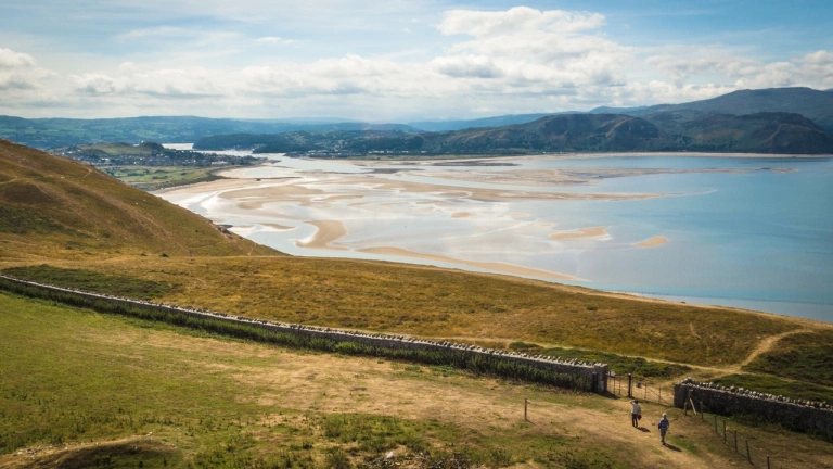 A coastal scene with blue sea and sand next to a green mountain