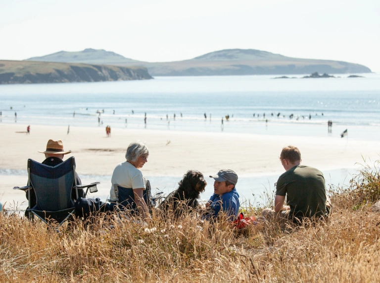 A group of people sitting on the sand looking out to sea.