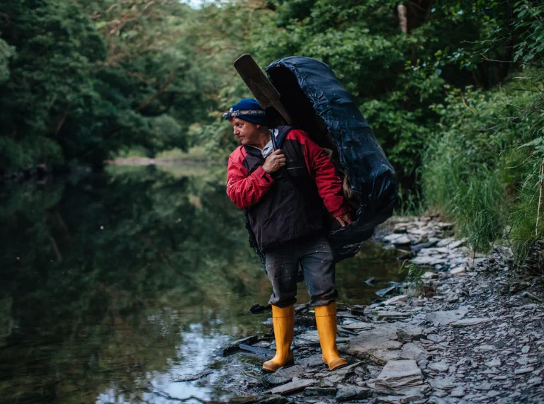 man carrying coracle stood on river bank
