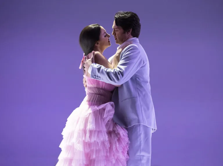 Two opera singers performing onstage in a romantic embrace